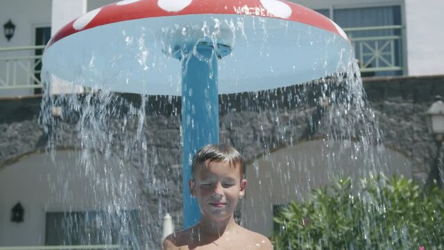 A portrait of a boy, standing under an outdoor aquapark shower, in the shape of a mushroom