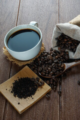 A cup of coffee, coffe beans and coffee powder on a wooden surface
