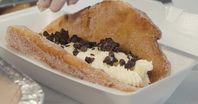 Sprinkling chocolate chips on a fried ice cream dessert. A gloved food truck worker sprinkles chocolate chunks on a decadent, sweet dessert with a crunchy fried shell, ice cream and whipped cream.