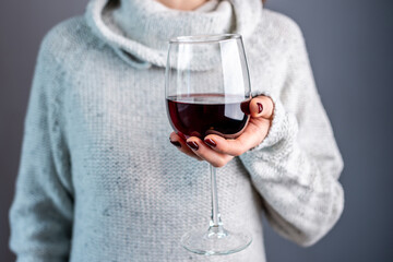 A woman in a white sweater is holding a glass of red wine in her hand. Close up