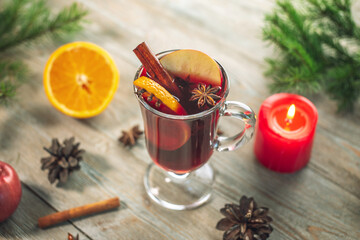 A glass cup with mulled wine decorated with cinnamon, star anise and fruit on a wooden table. Concept of a traditional hot winter beverage