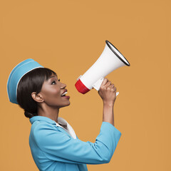 Cheerful young african stewardess shouts into the loudspeaker. Orange background.