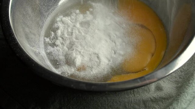 The flour slowly falls into the bowl with the chicken egg. Useful dough for baking. Slow motion.