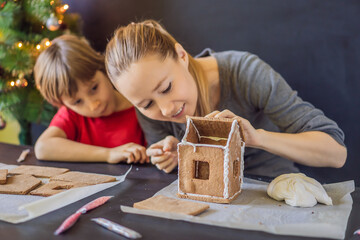 Young mother and kid making gingerbread house on Christmas eve