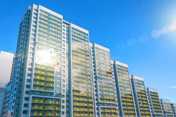 Fototapeta premium Multi-storey residential complex with sun glare, and a construction cradle by workers for finishing the external facade.