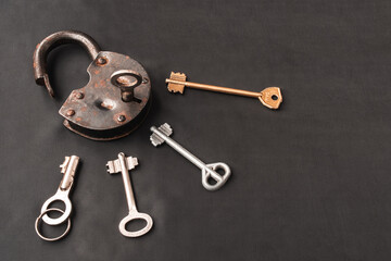 Opened old rusty lock with key in keyhole and many keys lying around on black background. Copy space. looking for problem solution concept