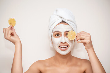 Funny smiling woman with white moisturizing mask holding orange piece. Beauty facial mask, skin care and treatment concept