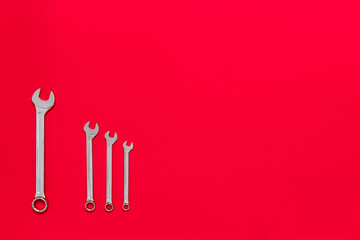 Four metal wrenches of different sizes isolated on red background with copy space. Conceptual idea of the differences between: boss and employee, older and younger, big and small, parent and child