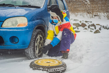 Winter accident on the road. A man changes a wheel during a snowfall wear medical masks due to the COVID-19 coronavirus. Winter problems