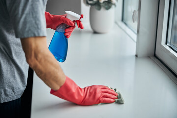 Responsible man cleaning and disinfecting surface of window-sill