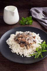 Risotto with mushrooms on a black plate. Boiled white rice with champignons in cream sauce. Dark wooden background.