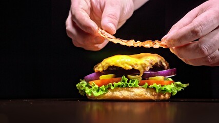 Craft burger is cooking on black background. Consist: sauce, lettuce, tomato, red onion, pickle, cheese, bacon, air bun and marbled meat beef. Not made ideal. Looks real, loving hand made.