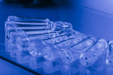 Glass medical ampoule vial for injection. Medicine is liquid sodium chloride with of aqueous solution in ampulla. Close up. Bottles ampule multicolor on background color and water. Human plasma.