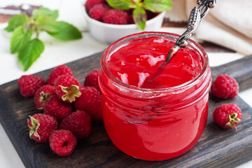 Homemade raspberry jam in a glass jar and fresh raspberries with mint on a wooden rustic background. Close up.