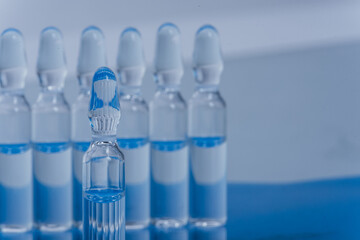 Glass medical ampoule vial for injection. Medicine is liquid sodium chloride with of aqueous solution in ampulla. Close up. Bottles ampule multicolor on background color and water. Human plasma.