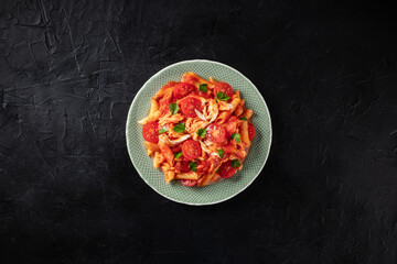 Penne pasta with chicken, tomato sauce and parsley leaves, overhead shot on a dark background