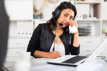 Portrait of disappointed crying female customer support phone operator with headphones during work in call center