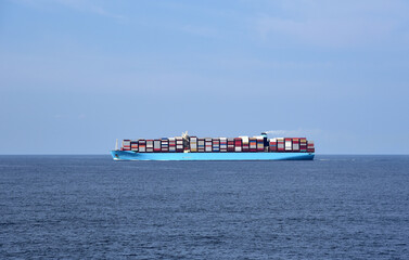 Fully loaded, large cargo container ship sailing through calm Indian Ocean on a sunny day.