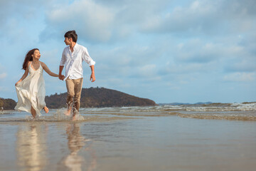 Young couple holding hands and running on the beach.