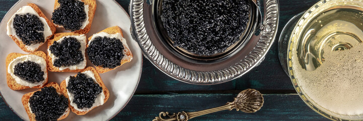 Black caviar panorama, overhead flat lay shot. Caviar on toasts and in a vintage bowl, with a champagne coupe