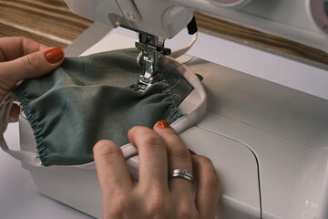 Naklejka premium Woman sewing cloth cotton face mask to protect from corona virus. Homemade handicraft protective mask against covid 19. 