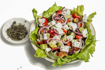 Greek salad in a plate with herbs and a bowl of oregano on a white background