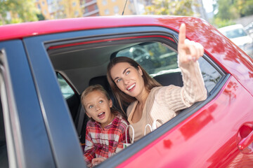 Girl looking out the window on backseat of car with her mom pointing upwards