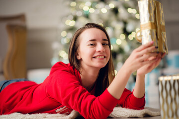 Beautiful happy young woman lying on the floor holding a Christmas present