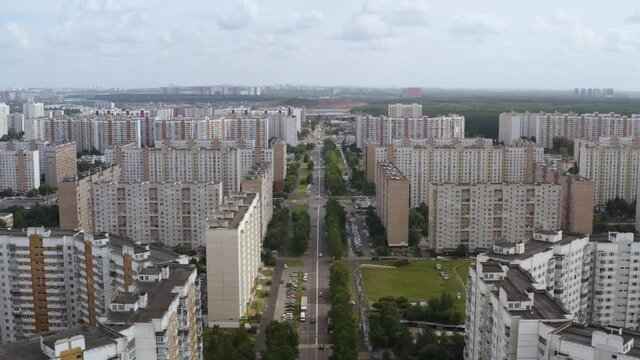 drone shooting city with multi-storey buildings and long road with green streen