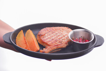 Rib eye steak served with baked potatoes and cranberry sauce on a black tray. In hands of waiter. Restaurant service.