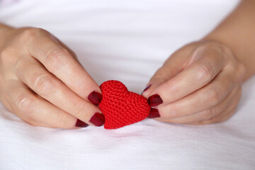 Red knitted heart in female hands on a bed. Concept of love, Valentines day celebration,...