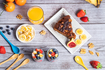 Gran desayuno al completo, con chia, pastel de chocolate con nueces y plátanos decorados con copos de avena, zumo de naranja, fresas y nueces