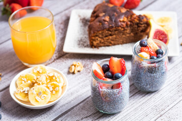 Dos vasos de chia con fresas y arándanos, pastel de chocolate con zumo de naranja y plátano con copos de avena