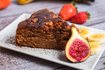 Pastel de chocolate con nueces decorado con higos y fresas encima de un plato blanco y un fondo gris claro 