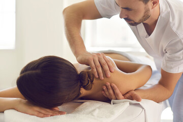 Obraz na płótnie Canvas Young masseur in physiotherapy center massaging woman's shoulder, easing pain and relaxing muscles