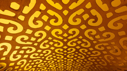 Decorative gold pattern close-up on the whole background. Arabic carved table lamp from the inside. Symmetrical design in warm colors.