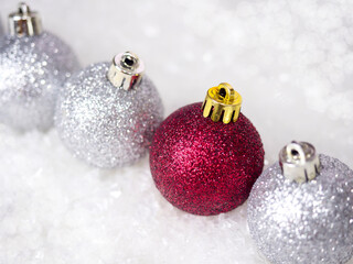 Three silver and one red Christmas balls in snow bokeh. View from above.