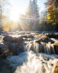 Mountain river in the morning with sun burst in fall autumn colors