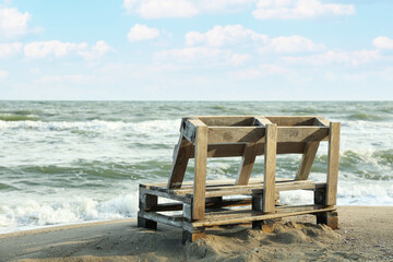 Wooden bench on sandy sea beach, space for text