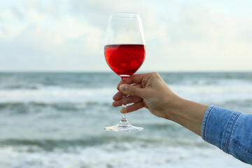Female hand hold glass of wine against sea