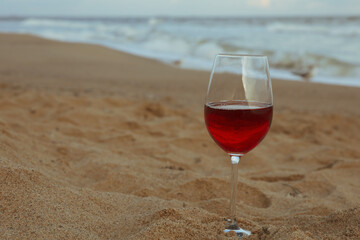 Glass of red wine on sandy sea beach