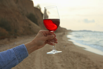 Female hand hold glass of wine on sandy beach