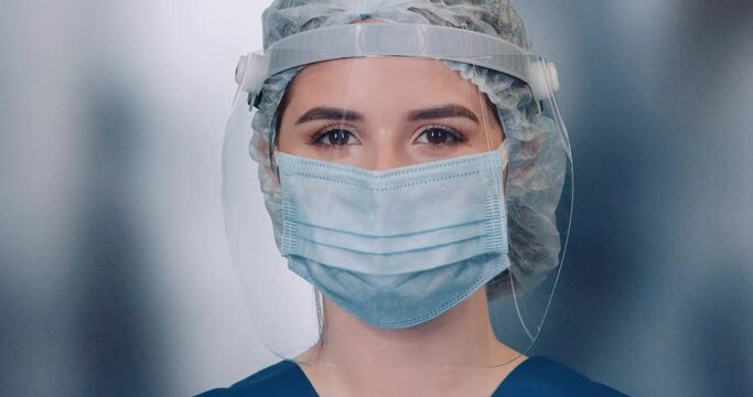 Portrait of young doctor female in protective gear and medical mask, woman looks at the camera and smiles, protection from a virus.