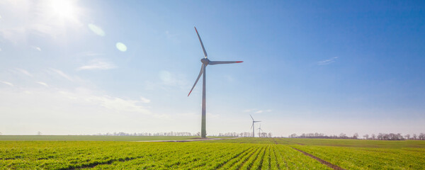 wind turbine on green field with sun flare blue sky background