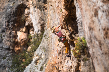 A strong woman climbs a beautiful orange rock.