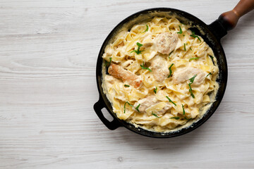 Homemade Chicken Fettuccine Alfredo in a cast-iron pan on a white wooden background, overhead view. Flat lay, top view, from above. Space for text.