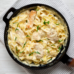 Homemade Chicken Fettuccine Alfredo in a cast-iron pan on a white wooden table, top view. Flat lay, overhead, from above. Close-up.