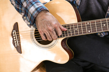Senoir man sitting and playing acoustic guitar.