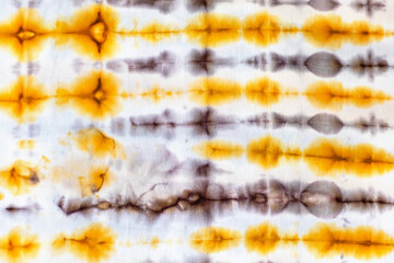 textile background - abstract yellow and brown ornament in tie-dye batik technique on white silk fabric of handcrafted scarf