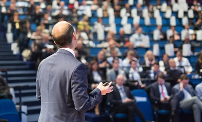 Rear view of speaker giving a talk on corporate business conference. Unrecognizable people in audience at conference hall. Business and Entrepreneurship event.